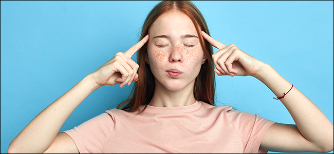 Uma garota com os olhos fechados, segurando os dedos indicadores nas têmporas.