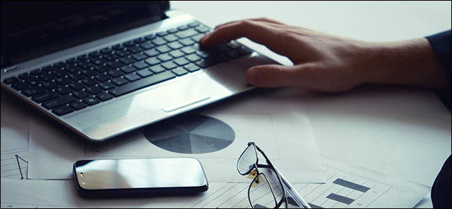 Um homem em uma mesa com seu telefone, laptop e óculos