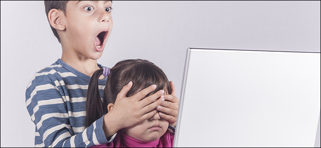 Um garotinho cobre os olhos da irmã no computador.