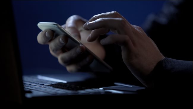 Mão segurando um smartphone em um quarto escuro.