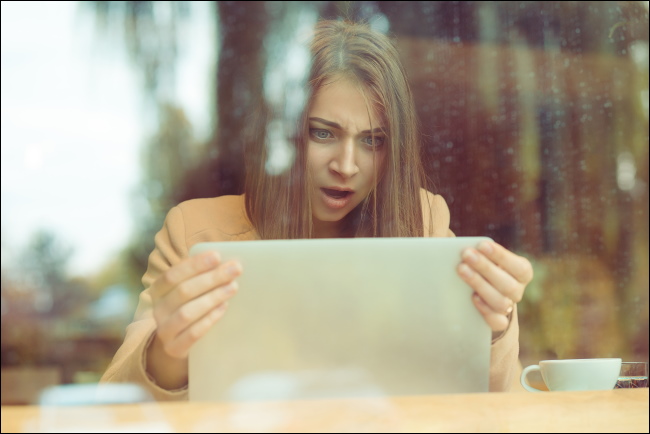 Uma mulher chocada segurando a tela de seu laptop.