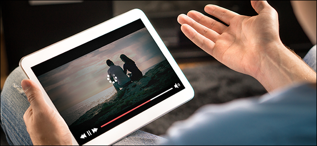 Mãos de um homem segurando um tablet exibindo um ícone de "carregamento" em um vídeo.