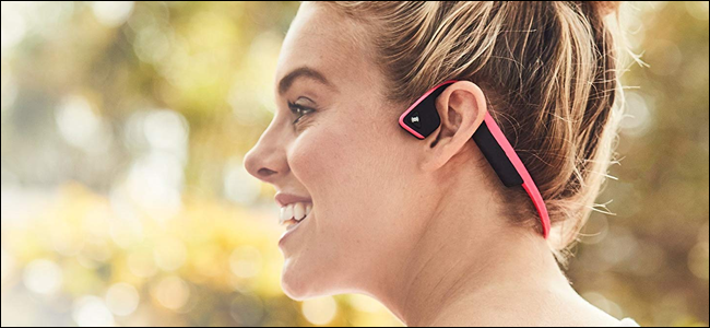 Uma mulher usando fones de ouvido de condução óssea AfterShokz.  Parece que ela está se divertindo, mas pode estar repreendendo um transeunte.