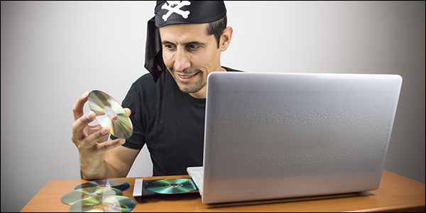 homem vestido de pirata sorrindo enquanto coloca um CD dentro de seu laptop