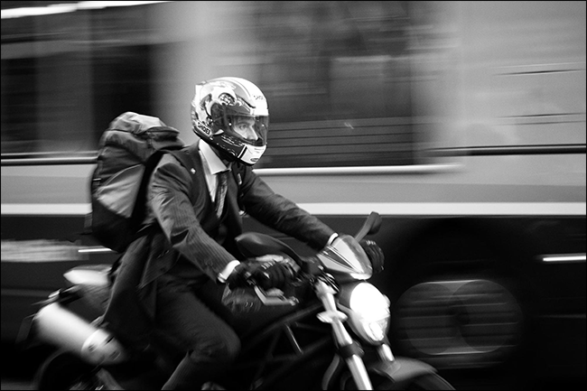 homem de terno andando de moto com ônibus borrado se movendo atrás dele