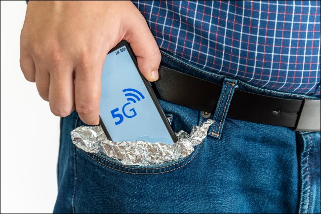 Um homem colocando um smartphone 5G em seu bolso coberto de papel alumínio.