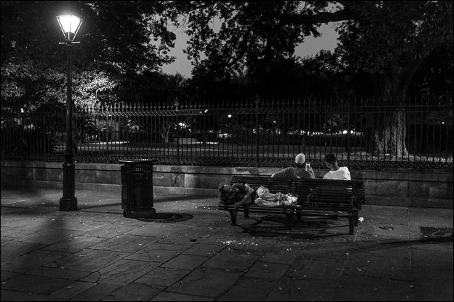 dois homens sentados no banco do parque à noite;  um homem dormindo no assento atrás deles