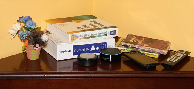 Um botão Echo e Echo em uma mesa de cabeceira perto de um celular, livros e uma planta.