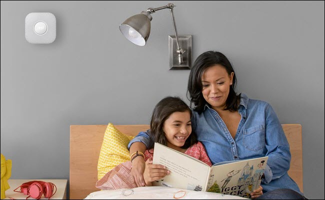 Mãe e filho lendo um livro infantil na cama, com um Nest Protect montado na parede acima de suas cabeças.