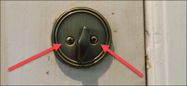 Um botão giratório padrão em uma fechadura, com duas setas vermelhas apontando para dois parafusos.