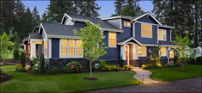 Exterior de uma casa azul e branca de dois andares ao anoitecer com as luzes internas acesas. 