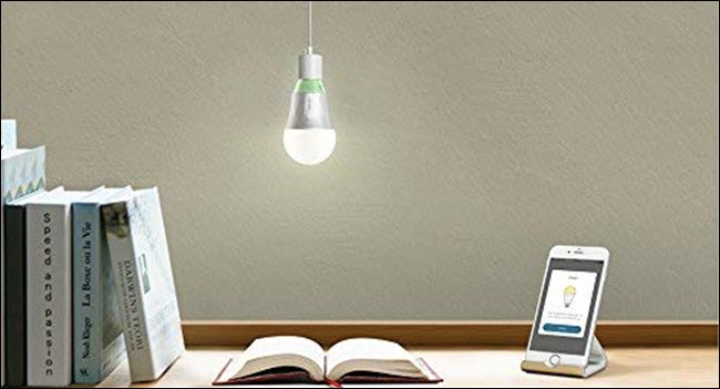 Uma lâmpada TP-Link Wi-Fi pendurada sobre um livro aberto e um telefone celular em uma mesa.