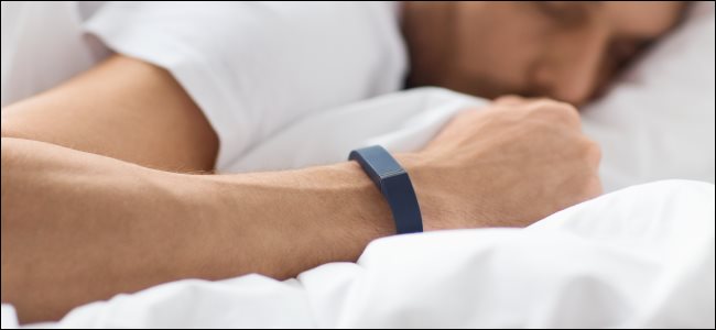 Um homem usando um rastreador de atividade no pulso enquanto dormia na cama.