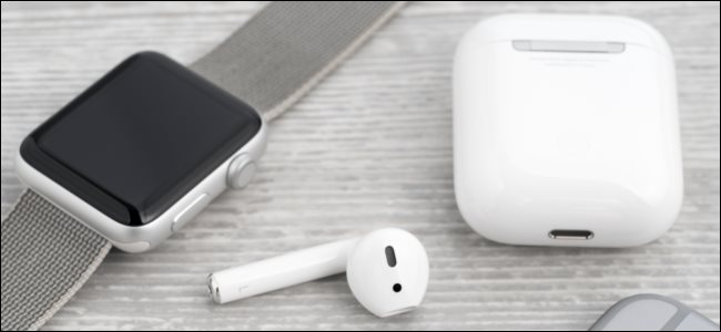 AirPods e seu estojo de carregamento ao lado de um Apple Watch.