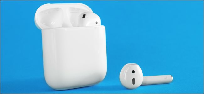 Um Apple AirPod no estojo de carregamento e o outro deitado ao lado dele. 