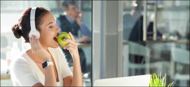 Uma mulher usando fones de ouvido enquanto usa um Apple Watch e come uma maçã.