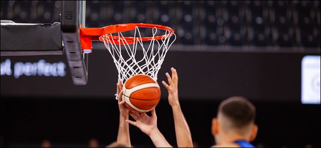 Mãos alcançando uma bola de basquete na frente da rede.