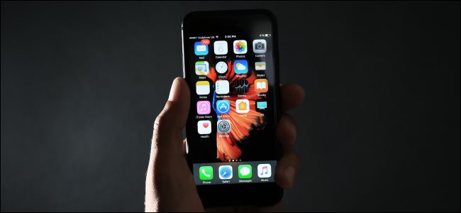 Uma mão segurando um iPhone preto no escuro.