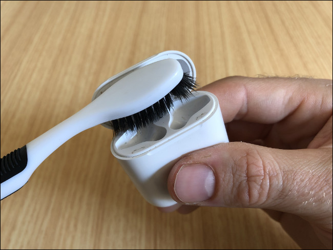 Mão de um homem segurando um estojo de carregamento de AirPods e limpando-o com uma escova de dentes.