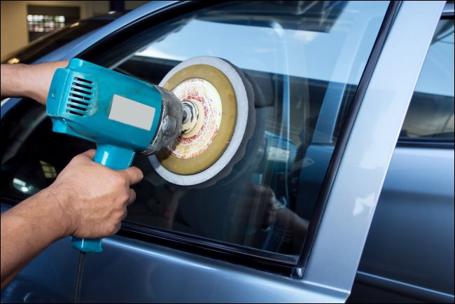 Mãos de um homem polindo uma janela de carro com uma máquina de buffer de energia.