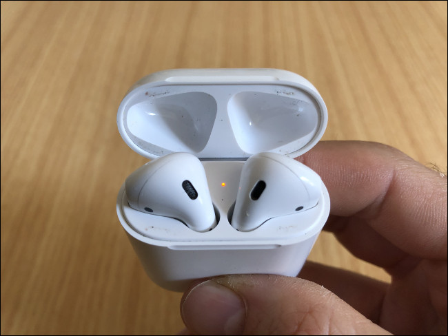 A mão de um homem segurando um par de AirPods em seu estojo de carregamento.