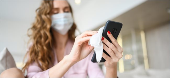 Uma mulher limpando um smartphone enquanto usava uma máscara facial.