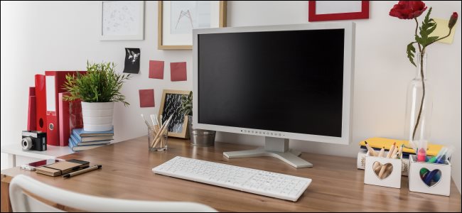 Um monitor de computador desktop e teclado em uma mesa de madeira em um escritório doméstico.
