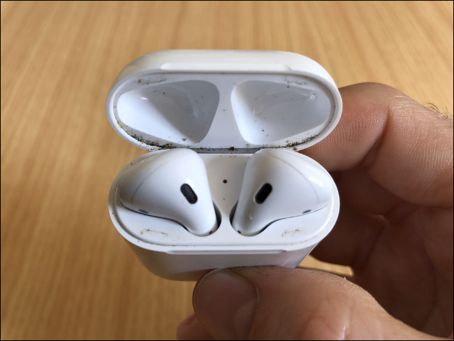 Uma mão segurando AirPods sujos em sua caixa igualmente suja.