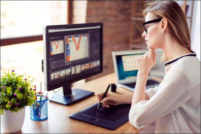 Uma mulher olhando para a tela de um computador enquanto desenha em um tablet digital.