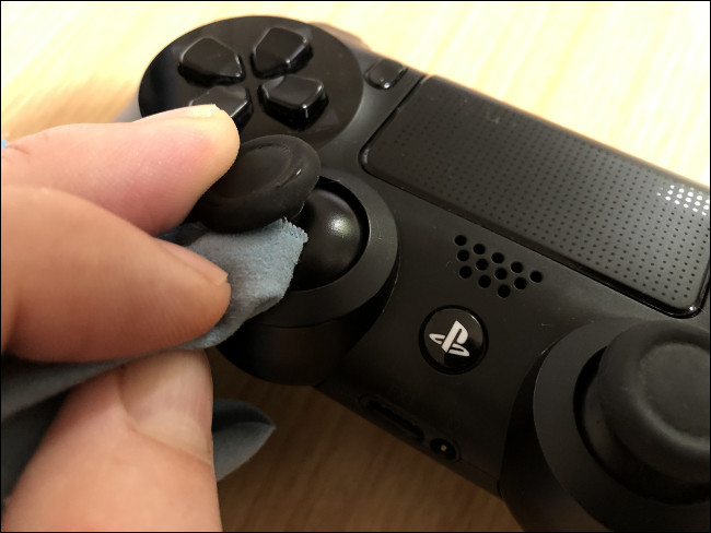 Uma mão limpando um stick analógico com um pano em um Controlador DualShock 4.
