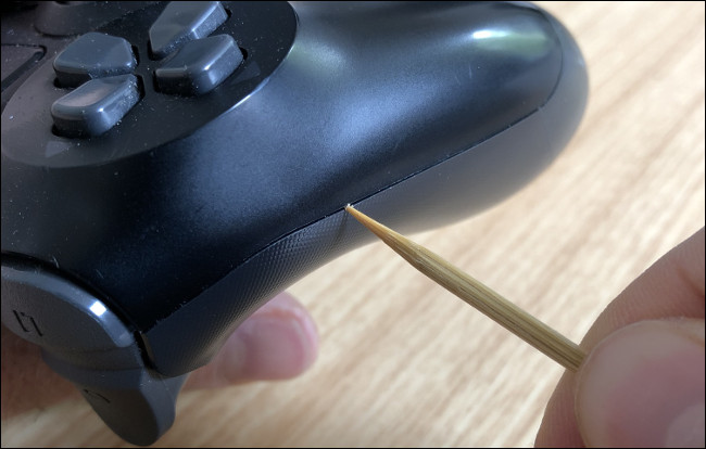 Uma mão limpando uma fenda na lateral de um DualShock 4 com um palito.