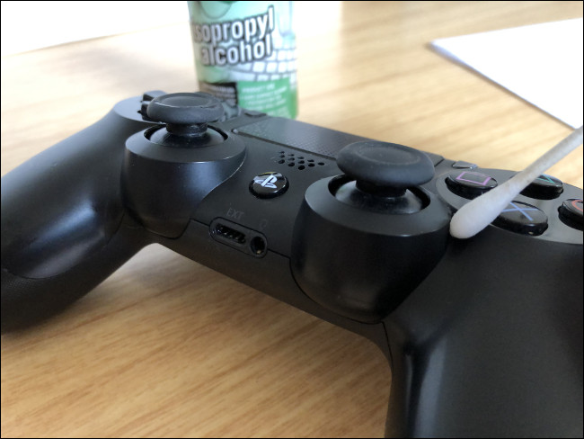 Um Controlador DualShock 4 com um cotonete em cima ao lado de uma garrafa de álcool isopropílico.