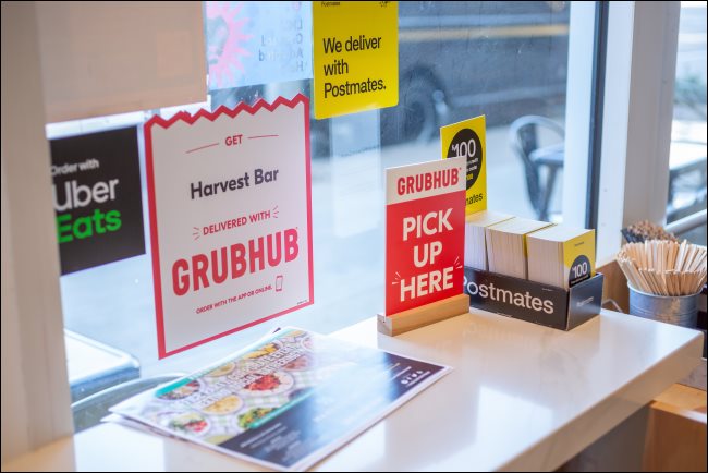 Sinais para GrubHub, Postmates e Uber Eats em um restaurante.