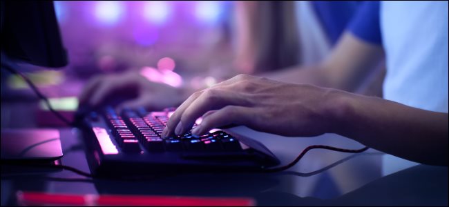Mãos em um teclado gamer de PC iluminado em luz roxa.