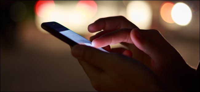 Um close-up de mãos usando um smartphone à noite na rua.