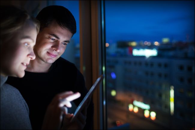 Duas pessoas olhando para um tablet brilhante no escuro