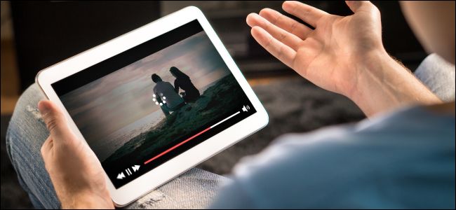 Mãos de homem segurando um tablet mostrando vídeo de armazenamento em buffer.