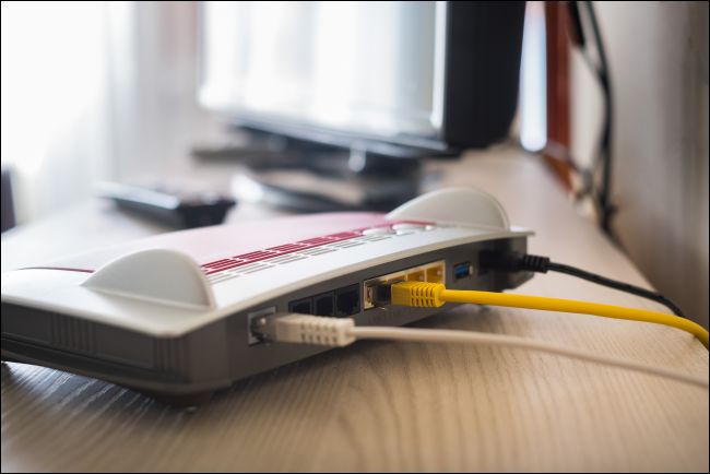 Cabos conectados à parte traseira de um modem que está localizado em uma mesa ao lado de um computador.