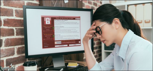 Mulher que parece chateada, sentada ao lado de um monitor de computador com ransomware nele.