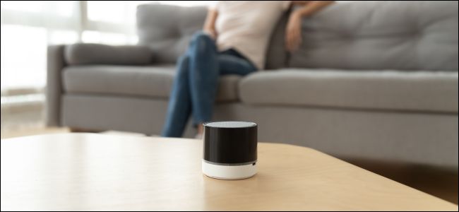 Um alto-falante Bluetooth sem fio em uma mesa de centro na frente de uma mulher sentada em um sofá.