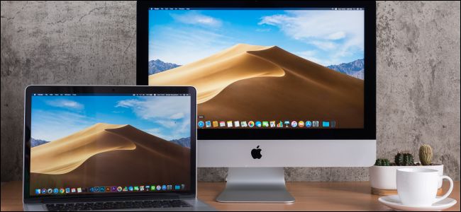 Um MacBook próximo a um iMac em uma mesa de madeira.