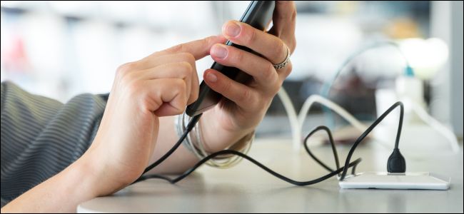 Mãos usando um telefone conectado a uma porta USB em uma estação de carregamento.