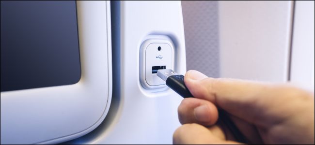 Uma mão conectando um cabo USB a uma porta de carregamento na parte traseira de um assento de avião.