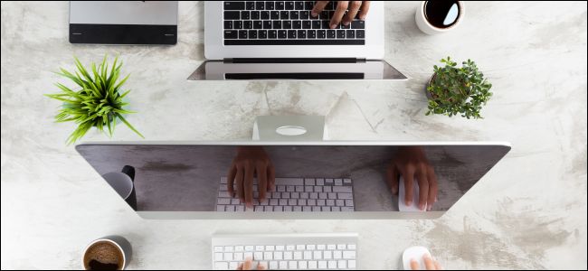As mãos de uma pessoa usando um Mac enquanto as mãos de outra pessoa usam um MacBook Pro do outro lado da mesa.