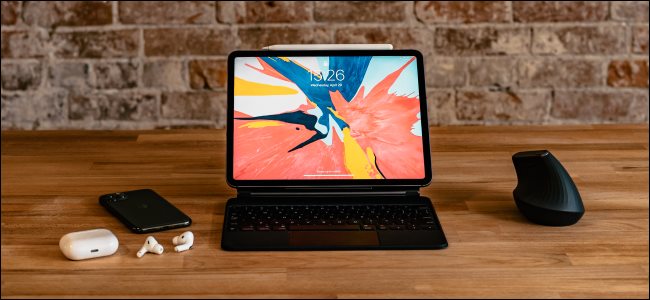 Um iPad Pro com teclado mágico, mouse, iPhone 11 Pro e AirPods em uma mesa.