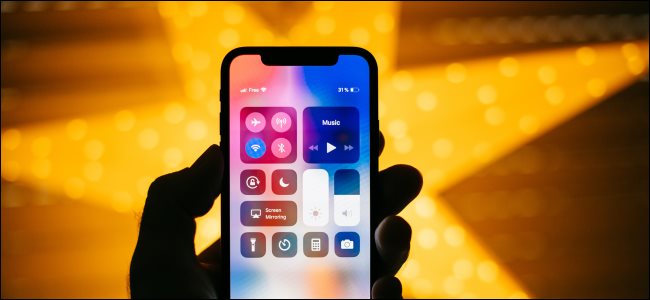 Uma mão segurando um iPhone X com o Control Center aberto.