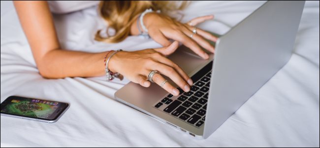 Uma mulher usando um MacBook em uma cama, o que é ruim para o resfriamento.