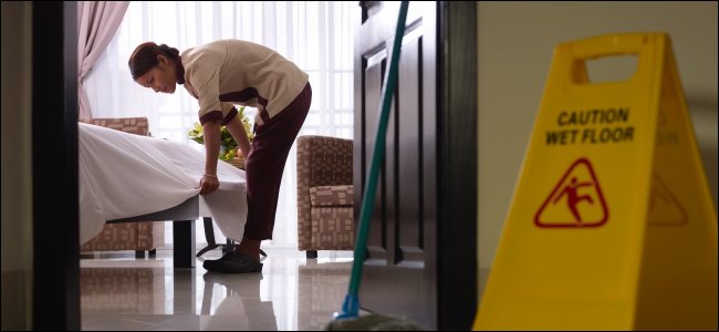 Uma empregada arrumando uma cama em um quarto de hotel.