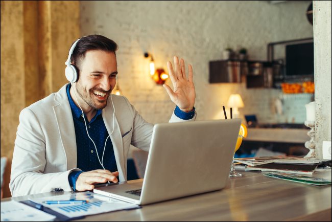 Um homem usando fones de ouvido e acenando para seu laptop.