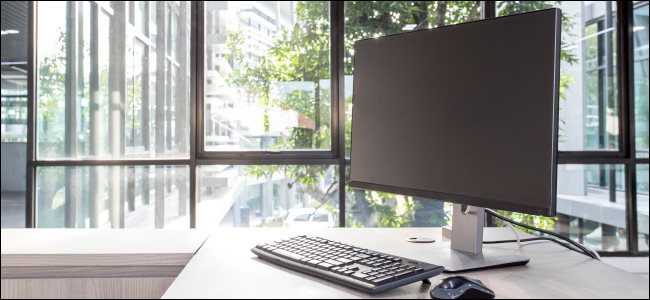 Um monitor de PC, teclado e mouse em uma mesa de escritório.